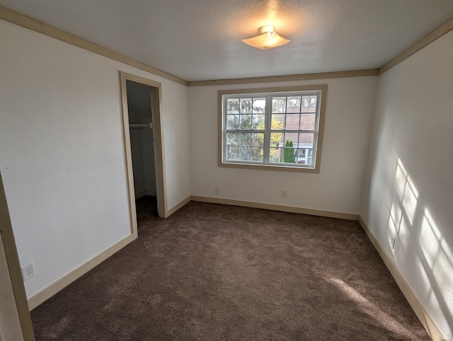 unfurnished bedroom with a closet, ornamental molding, a walk in closet, and dark colored carpet