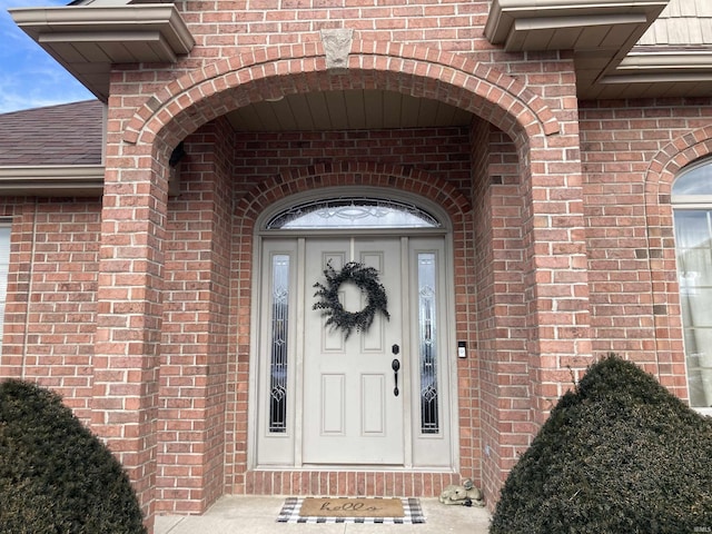 view of exterior entry with brick siding and roof with shingles