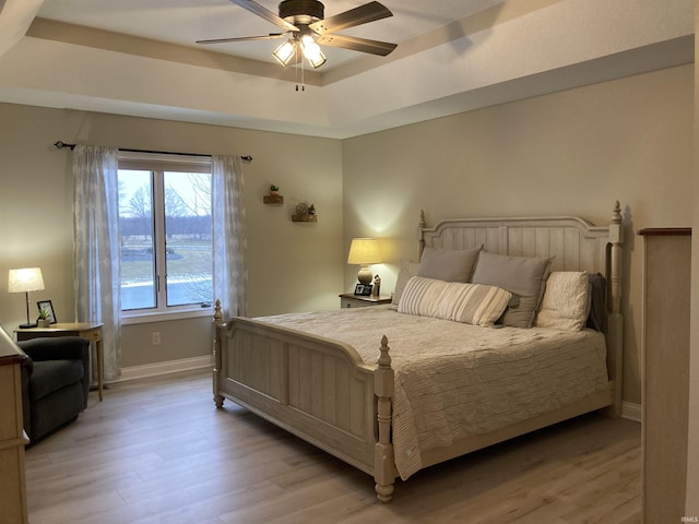 bedroom featuring ceiling fan, light hardwood / wood-style floors, and a tray ceiling