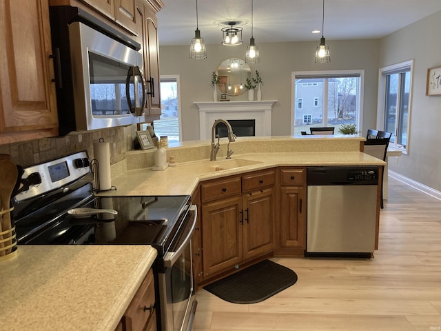 kitchen with light wood-style flooring, a fireplace, a sink, stainless steel appliances, and light countertops