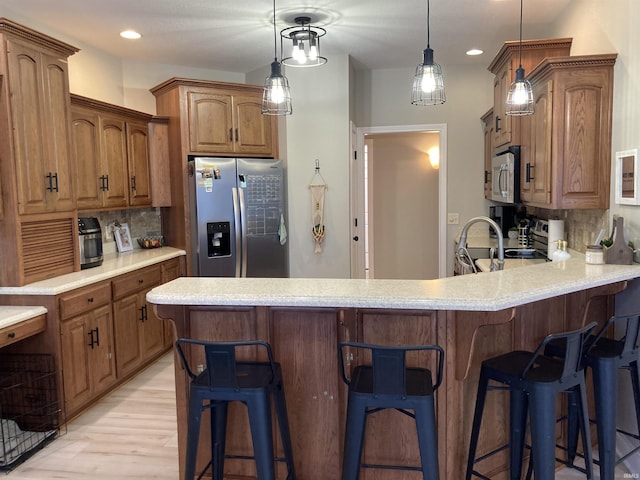 kitchen with backsplash, a kitchen bar, light countertops, a peninsula, and stainless steel appliances