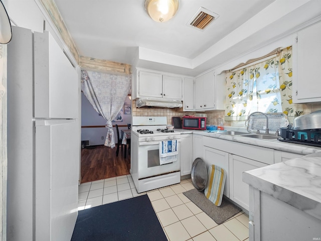 kitchen with backsplash, white appliances, white cabinetry, and light tile patterned floors