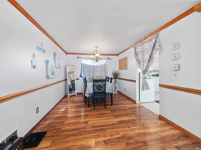 dining space featuring hardwood / wood-style flooring, washer / dryer, ornamental molding, and an inviting chandelier