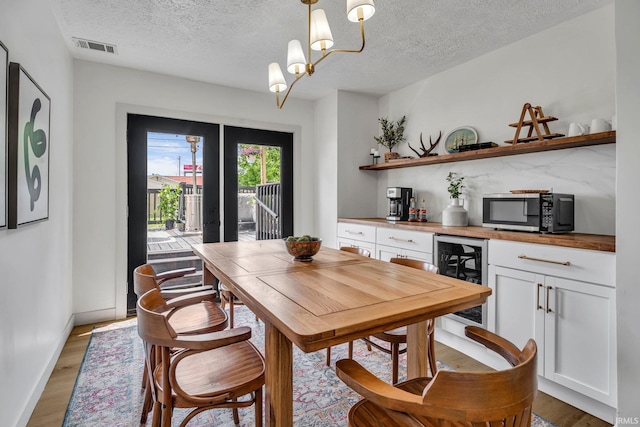 dining space with wood-type flooring, a textured ceiling, a notable chandelier, and beverage cooler