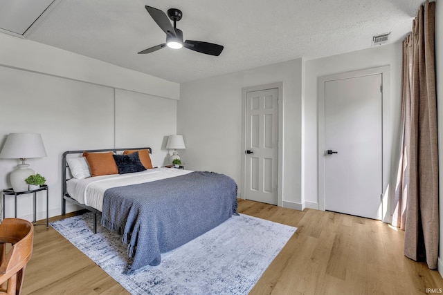 bedroom with ceiling fan, light hardwood / wood-style floors, and a textured ceiling