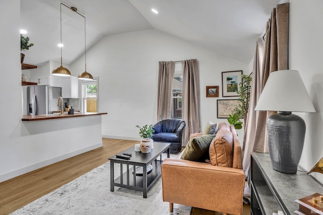 living room with sink, light hardwood / wood-style flooring, and vaulted ceiling