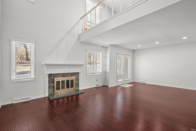 unfurnished living room with a high ceiling, a tile fireplace, a textured ceiling, and wood-type flooring