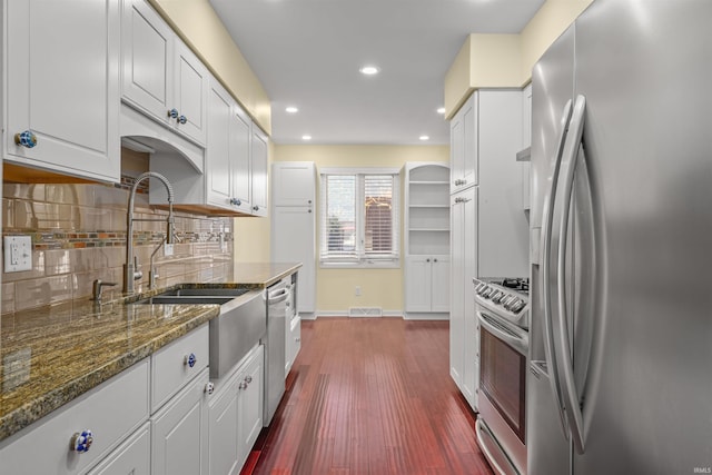 kitchen featuring appliances with stainless steel finishes, white cabinetry, dark hardwood / wood-style floors, dark stone countertops, and decorative backsplash