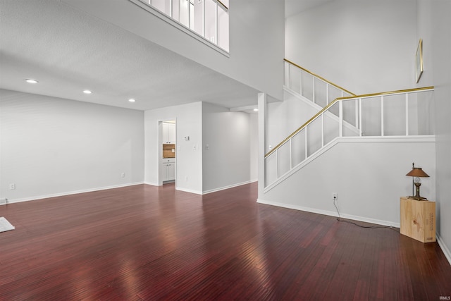 unfurnished living room with dark wood-type flooring, a textured ceiling, and a high ceiling