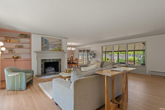 living room with light hardwood / wood-style floors, a baseboard heating unit, a high end fireplace, and a chandelier