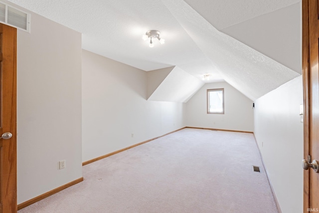 additional living space featuring vaulted ceiling, light colored carpet, and a textured ceiling