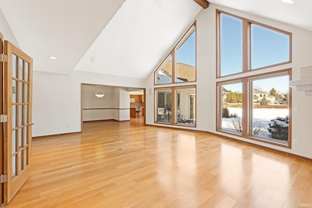 unfurnished living room with high vaulted ceiling, light hardwood / wood-style floors, beamed ceiling, and a healthy amount of sunlight