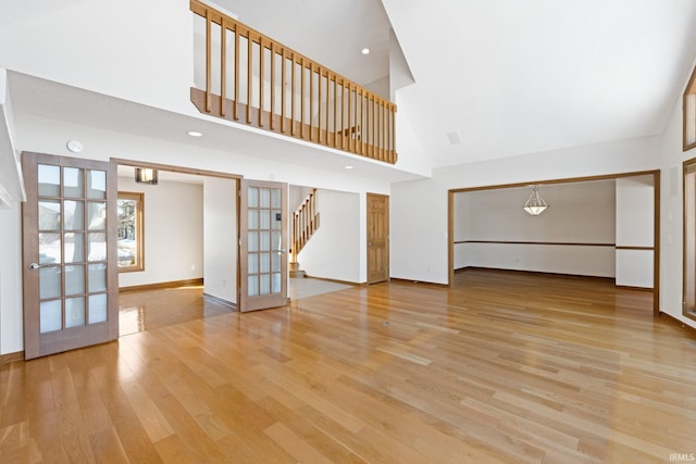 unfurnished living room featuring french doors, a high ceiling, and light hardwood / wood-style floors