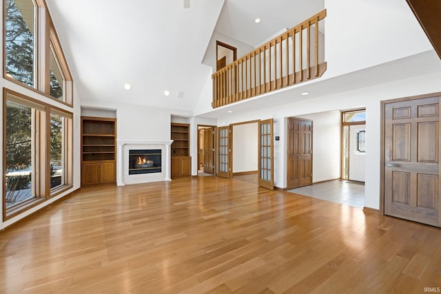 unfurnished living room with built in shelves, light hardwood / wood-style flooring, high vaulted ceiling, and french doors