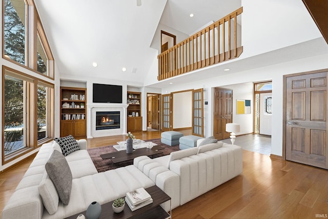 living room with a high ceiling, built in shelves, light hardwood / wood-style flooring, and french doors