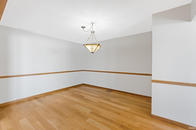 empty room with an inviting chandelier and light hardwood / wood-style flooring