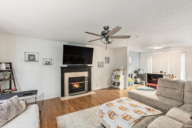 living room featuring hardwood / wood-style flooring, ceiling fan, and a tiled fireplace