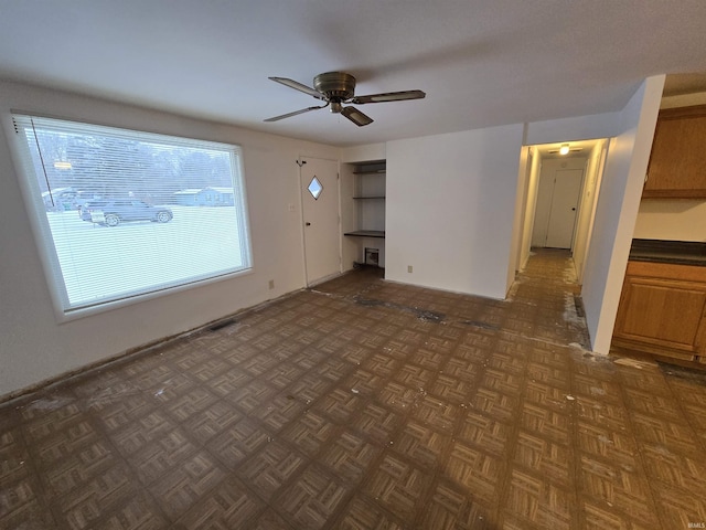 unfurnished living room featuring ceiling fan and dark parquet flooring