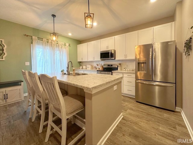 kitchen with sink, hanging light fixtures, appliances with stainless steel finishes, an island with sink, and white cabinets