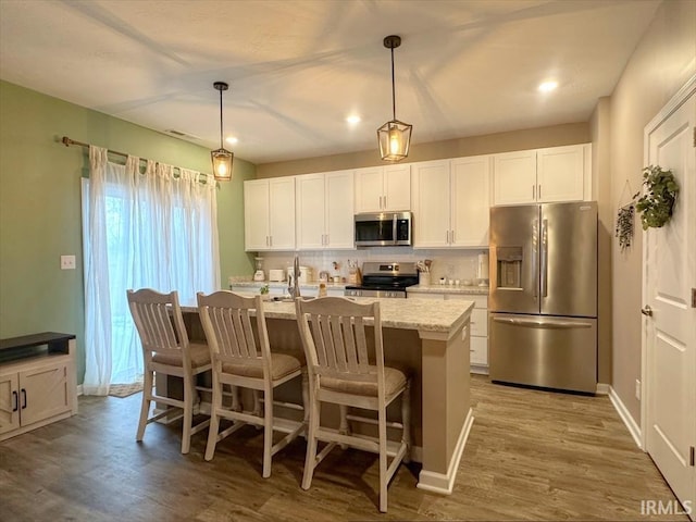 kitchen featuring white cabinetry, stainless steel appliances, an island with sink, and hanging light fixtures