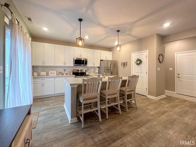 kitchen with hanging light fixtures, stainless steel appliances, light stone counters, white cabinets, and a center island with sink