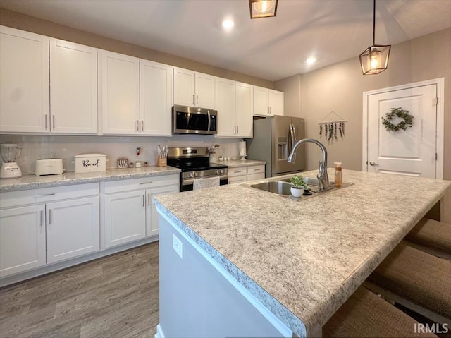 kitchen featuring appliances with stainless steel finishes, pendant lighting, white cabinetry, sink, and a kitchen island with sink