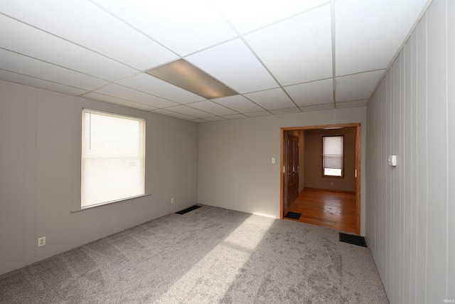 empty room with wood walls, carpet floors, and a drop ceiling