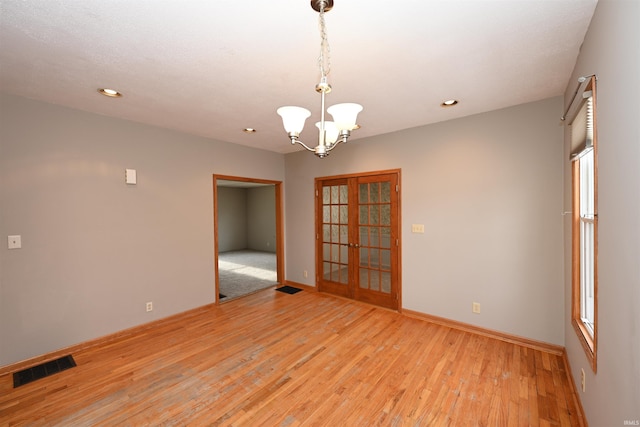 empty room featuring light hardwood / wood-style floors, a chandelier, and french doors