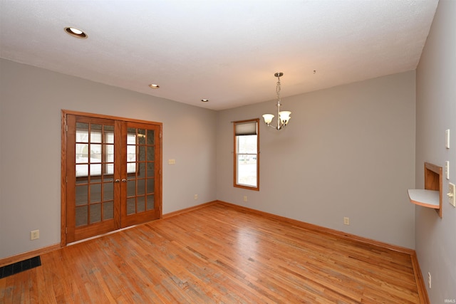 unfurnished room with light hardwood / wood-style floors, a notable chandelier, and french doors