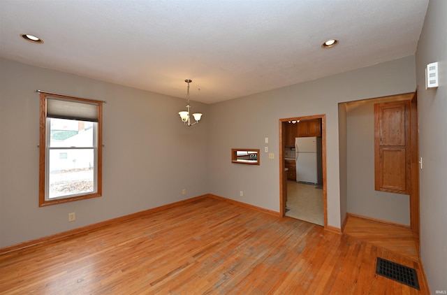 empty room with a chandelier and light wood-type flooring