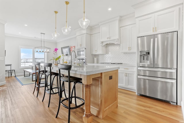 kitchen with decorative light fixtures, white cabinets, appliances with stainless steel finishes, and a center island with sink