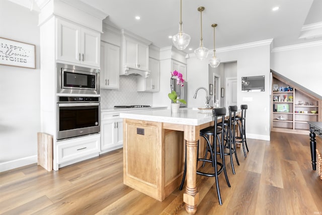 kitchen featuring decorative light fixtures, white cabinetry, stainless steel appliances, an island with sink, and sink