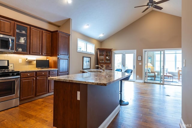 kitchen with sink, backsplash, high vaulted ceiling, an island with sink, and stainless steel appliances