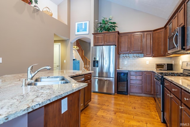 kitchen with wine cooler, appliances with stainless steel finishes, sink, light stone countertops, and high vaulted ceiling