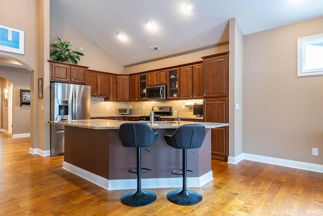 kitchen with a kitchen bar, appliances with stainless steel finishes, a kitchen island with sink, decorative backsplash, and light stone counters