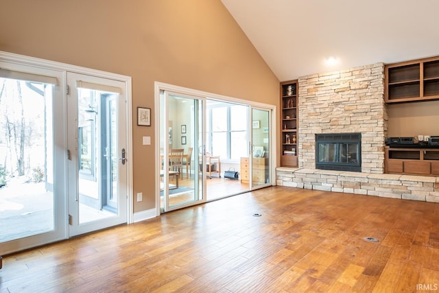 unfurnished living room with built in shelves, a stone fireplace, light hardwood / wood-style flooring, and a wealth of natural light