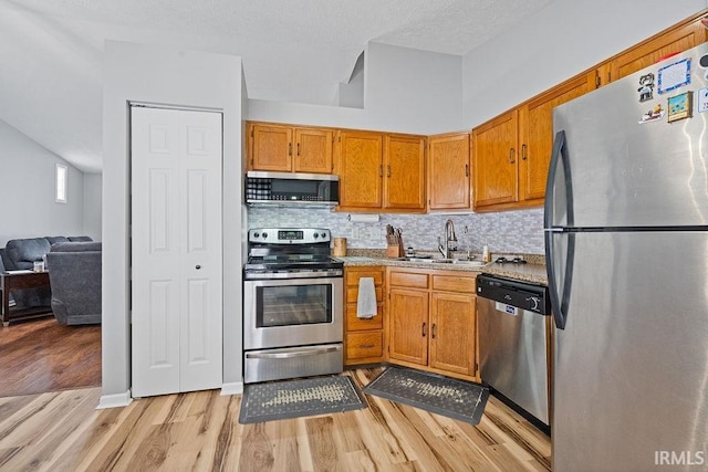 kitchen featuring sink, light wood-type flooring, stainless steel appliances, a high ceiling, and backsplash