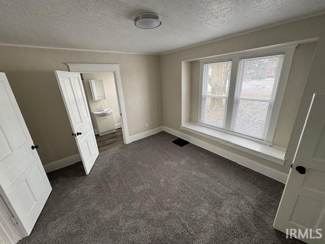 unfurnished bedroom featuring ensuite bathroom, dark colored carpet, and a textured ceiling