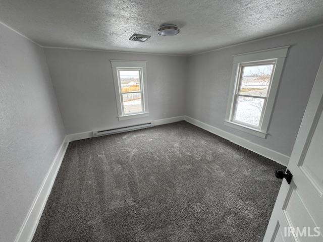 carpeted empty room with a healthy amount of sunlight, baseboard heating, and a textured ceiling