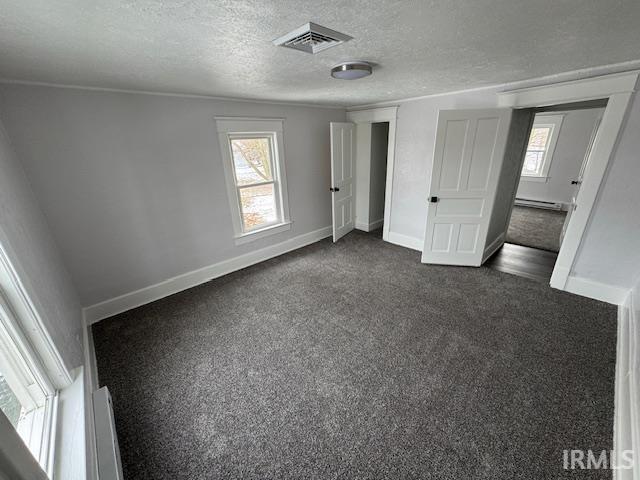 unfurnished bedroom with baseboard heating, a textured ceiling, and dark colored carpet