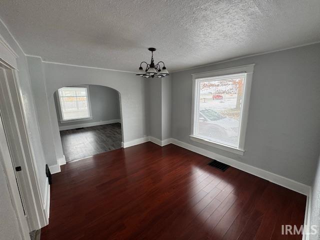 spare room with dark wood-type flooring, a textured ceiling, and a notable chandelier