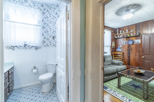 bathroom with wooden walls, toilet, and vanity