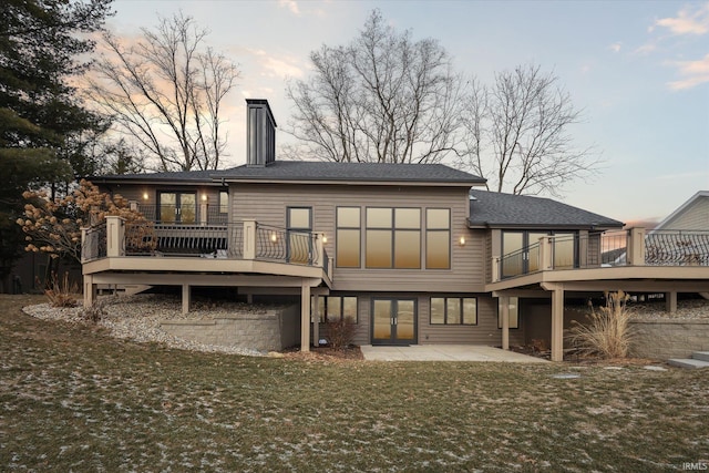 back house at dusk featuring a patio area, a deck, and a lawn