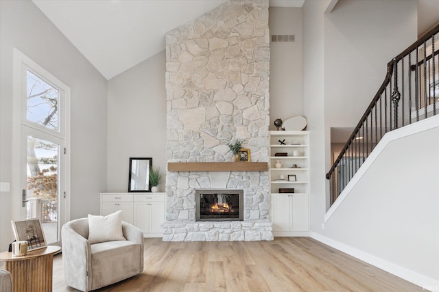 living room featuring high vaulted ceiling, light hardwood / wood-style flooring, and a stone fireplace