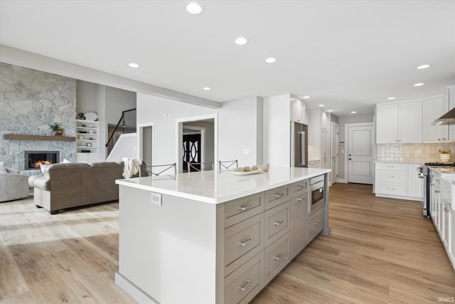 kitchen featuring white cabinetry, stainless steel appliances, a stone fireplace, tasteful backsplash, and a large island