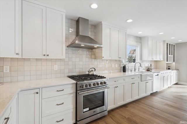 kitchen with sink, white cabinets, wall chimney exhaust hood, and stainless steel range