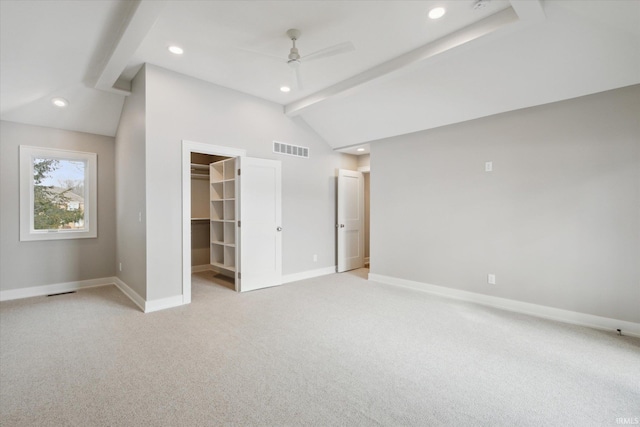 unfurnished bedroom featuring light carpet, ceiling fan, vaulted ceiling with beams, a spacious closet, and a closet