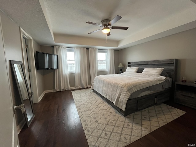 bedroom with ceiling fan, wood-type flooring, a tray ceiling, and a textured ceiling