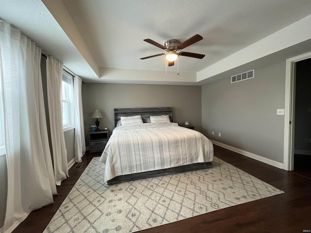 bedroom featuring ceiling fan, a textured ceiling, a tray ceiling, and dark hardwood / wood-style flooring