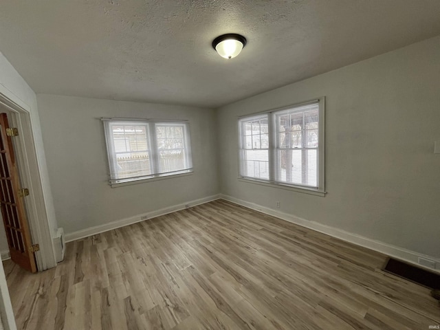 spare room featuring a healthy amount of sunlight, light hardwood / wood-style flooring, and a textured ceiling